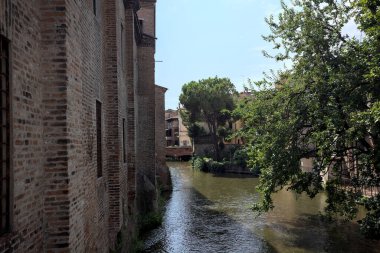 Güneşli bir günde, İtalya 'nın bir şehrinde, diğer tarafında ağaç olan tuğla bir binayla çevrili su akıntısı.