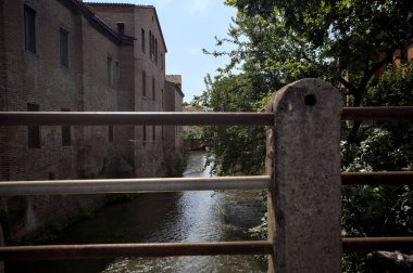 Güneşli bir günde, İtalya 'nın bir şehrinde, diğer tarafında ağaç olan tuğla bir binayla çevrili su akıntısı.