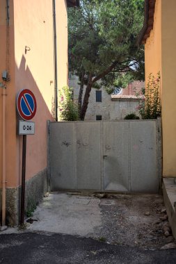 Güneşli bir günde deniz çamı ve arkasında binalar olan dar bir geçitte demir kapı.