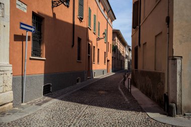Yol, binaların arasındaki mesafeye kadar uzanan gölgede kısmen kaldırımlı bir sokağa erişim.