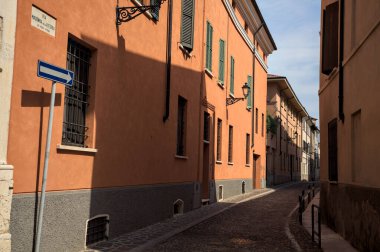 Yol, binaların arasındaki mesafeye kadar uzanan gölgede kısmen kaldırımlı bir sokağa erişim.