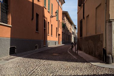 Yol, binaların arasındaki mesafeye kadar uzanan gölgede kısmen kaldırımlı bir sokağa erişim.