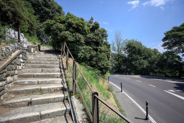 Güneşli bir günde etrafı ormanla çevrili bir uçurumun kenarındaki virajın yanındaki merdivende.
