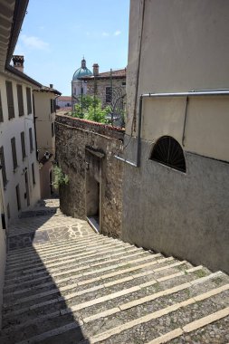 Güneşli bir günde arka planda bir kilisenin kubbesi olan bir binayla taş duvar arasında bir merdivenden yapılmış.
