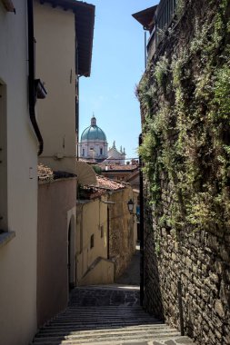 Güneşli bir günde arka planda bir kilisenin kubbesi olan bir binayla taş duvar arasında bir merdivenden yapılmış.