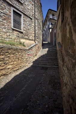 Güneşli bir günde, üzerinde sokak lambaları olan bir bina ile taştan bir cephenin arasındaki merdivenlere tırmanmak.
