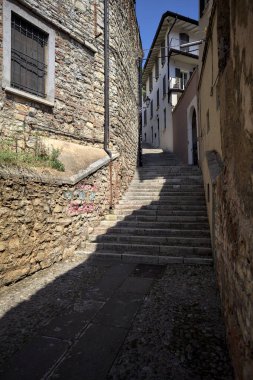 Güneşli bir günde, üzerinde sokak lambaları olan bir bina ile taştan bir cephenin arasındaki merdivenlere tırmanmak.