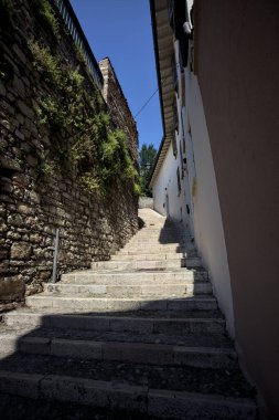 Güneşli bir günde, üzerinde sokak lambaları olan bir bina ile taştan bir cephenin arasındaki merdivenlere tırmanmak.