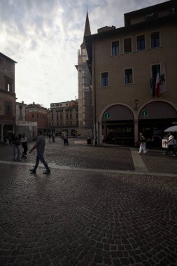 Mantova, Italy - 24TH AUGUST 2025 - Square in a town with people passing by next to a church and a porch at sunset