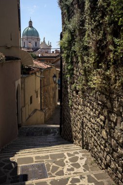 Brescia, Italy - 1ST AUGUST 2025 - Alley made of a staircase between a building and a stone wall with the dome of the Brescia basilica in the background on a sunny day
