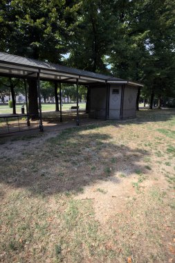 Closed kiosk in the shade under a few trees in a park on a sunny day