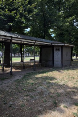 Closed kiosk in the shade under a few trees in a park on a sunny day
