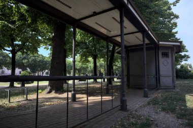 Closed kiosk in the shade under a few trees in a park on a sunny day
