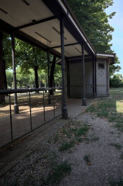 Closed kiosk in the shade under a few trees in a park on a sunny day