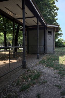 Closed kiosk in the shade under a few trees in a park on a sunny day