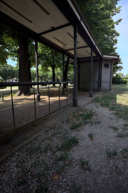 Closed kiosk in the shade under a few trees in a park on a sunny day