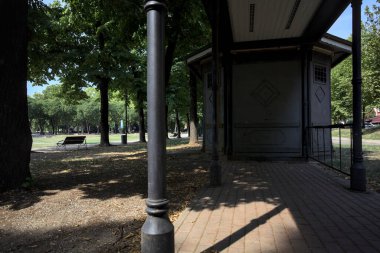 Closed kiosk in the shade under a few trees in a park on a sunny day