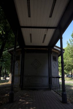 Closed kiosk in the shade under a few trees in a park on a sunny day