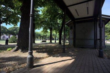 Closed kiosk in the shade under a few trees in a park on a sunny day