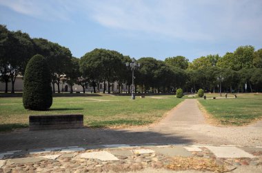 Opening forming a square with trails and bushes bordered by trees on it in a park on a sunny day