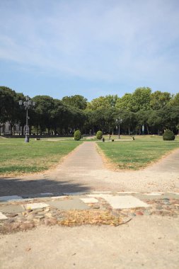 Opening forming a square with trails and bushes bordered by trees on it in a park on a sunny day