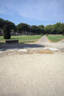 Opening forming a square with trails and bushes bordered by trees on it in a park on a sunny day