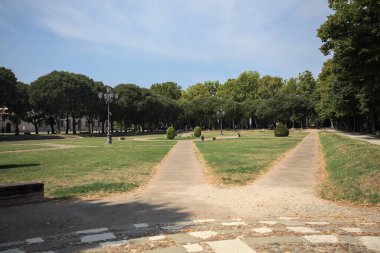 Opening forming a square with trails and bushes bordered by trees on it in a park on a sunny day