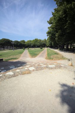 Opening forming a square with trails and bushes bordered by trees on it in a park on a sunny day