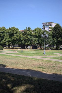 Opening forming a square with trails and bushes bordered by trees on it in a park on a sunny day
