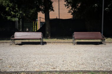 Ağaçların arkasındaki yolun kenarındaki banklar ve güneşli bir günde bir çit.