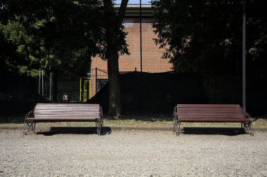 Ağaçların arkasındaki yolun kenarındaki banklar ve güneşli bir günde bir çit.
