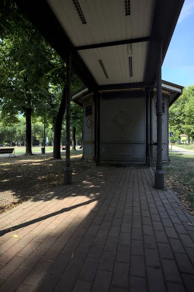 Closed kiosk in the shade under a few trees in a park on a sunny day