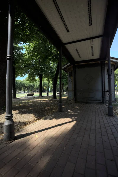 Closed kiosk in the shade under a few trees in a park on a sunny day