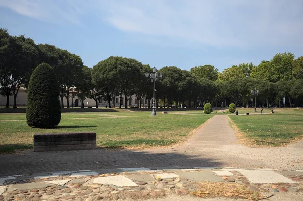 Opening forming a square with trails and bushes bordered by trees on it in a park on a sunny day