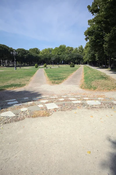Opening forming a square with trails and bushes bordered by trees on it in a park on a sunny day