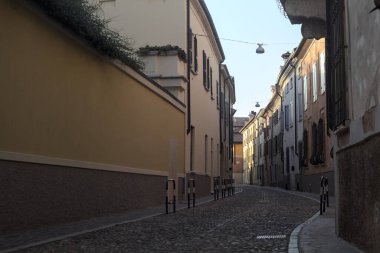 Yolun bir tarafındaki bir binanın balkonunda, gölgede kısmen boş bir cadde var.