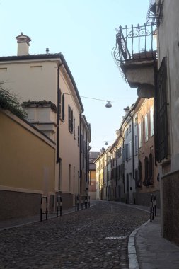 Yolun bir tarafındaki bir binanın balkonunda, gölgede kısmen boş bir cadde var.
