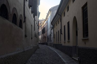 Gün batımında bir İtalyan kasabasının gölgesinde, kaldırımlı ve dar bir sokakta eğil.