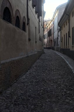 Gün batımında bir İtalyan kasabasının gölgesinde, kaldırımlı ve dar bir sokakta eğil.