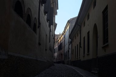 Gün batımında bir İtalyan kasabasının gölgesinde, kaldırımlı ve dar bir sokakta eğil.