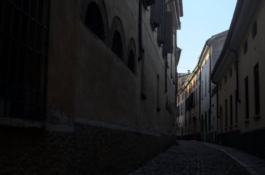 Gün batımında bir İtalyan kasabasının gölgesinde, kaldırımlı ve dar bir sokakta eğil.