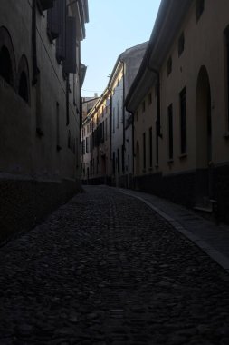 Gün batımında bir İtalyan kasabasının gölgesinde, kaldırımlı ve dar bir sokakta eğil.