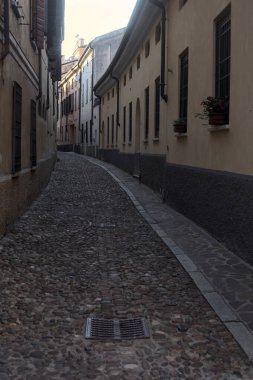 Gün batımında bir İtalyan kasabasının gölgesinde, kaldırımlı ve dar bir sokakta eğil.