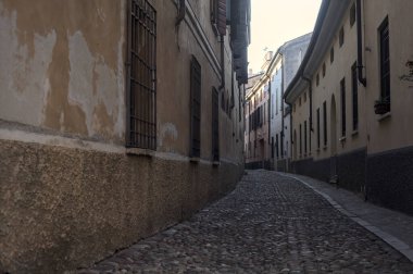 Gün batımında bir İtalyan kasabasının gölgesinde, kaldırımlı ve dar bir sokakta eğil.