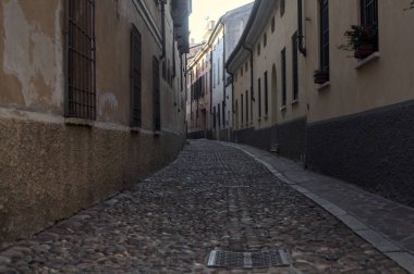 Gün batımında bir İtalyan kasabasının gölgesinde, kaldırımlı ve dar bir sokakta eğil.