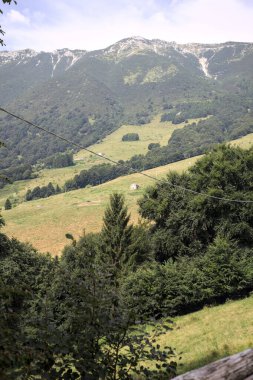 Dağların yamaçlarını noktalayan çayırlar ve ağaçlar, uzaklıktan görünen dağ sırtı ile birlikte.
