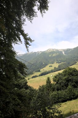 Dağların yamaçlarını noktalayan çayırlar ve ağaçlar, uzaklıktan görünen dağ sırtı ile birlikte.