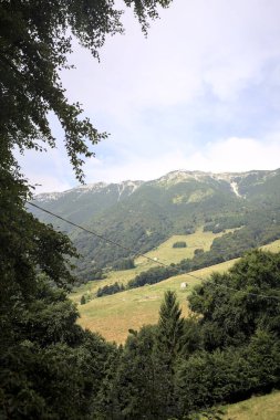 Dağların yamaçlarını noktalayan çayırlar ve ağaçlar, uzaklıktan görünen dağ sırtı ile birlikte.