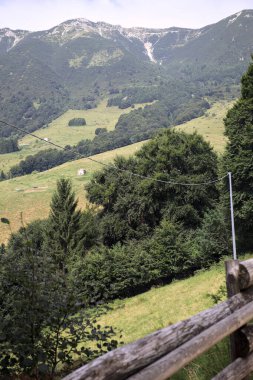 Dağların yamaçlarını noktalayan çayırlar ve ağaçlar, uzaklıktan görünen dağ sırtı ile birlikte.