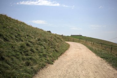 Güneşli bir günde, çayırlarla çevrili bir telle çevrili dağda yükselen patika.